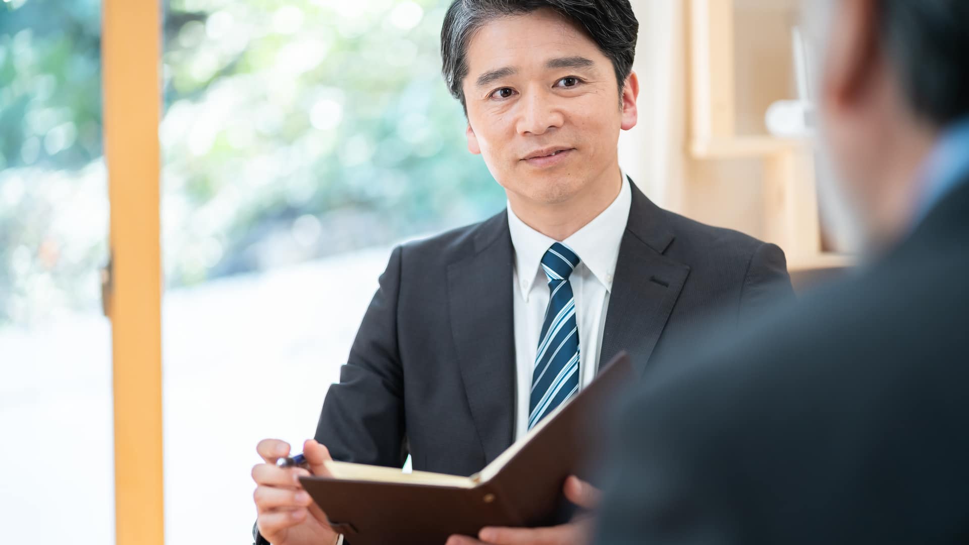 経営者のお話を、手帳を手に伺う場面